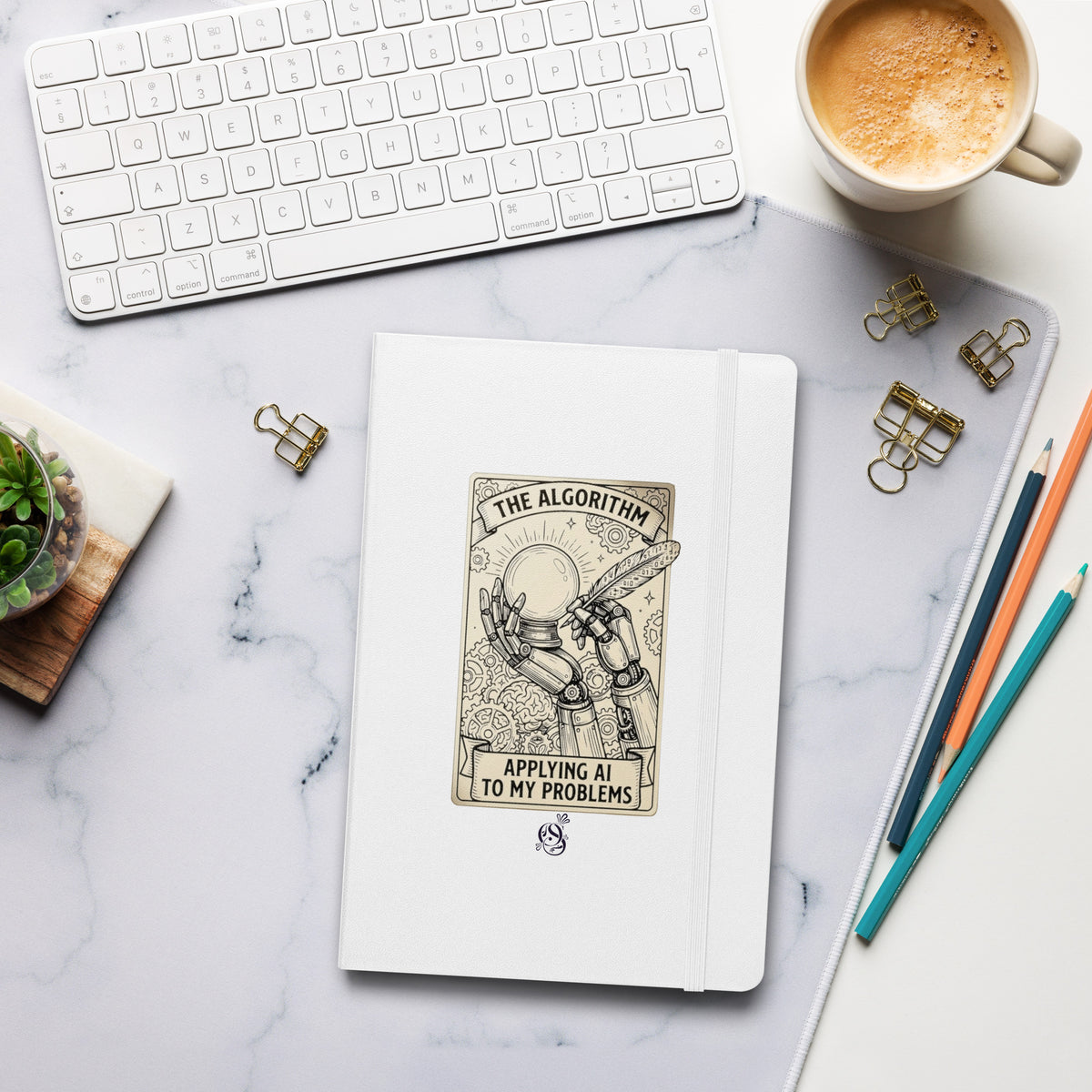 Matte white hardcover notebook on a desk beside a keyboard, coffee cup, and pens.