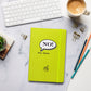 Chartreuse hardcover notebook lying on a desk beside a coffee cup and pens.
