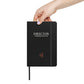 A hand holding the charcoal matte hardcover notebook.