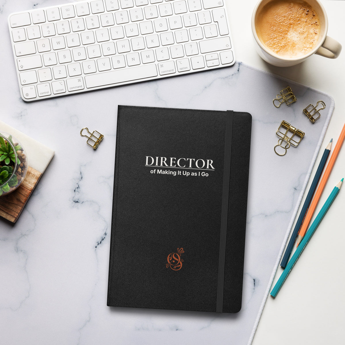 Charcoal matte hardcover notebook on a desk beside a keyboard, coffee cup, and pens.