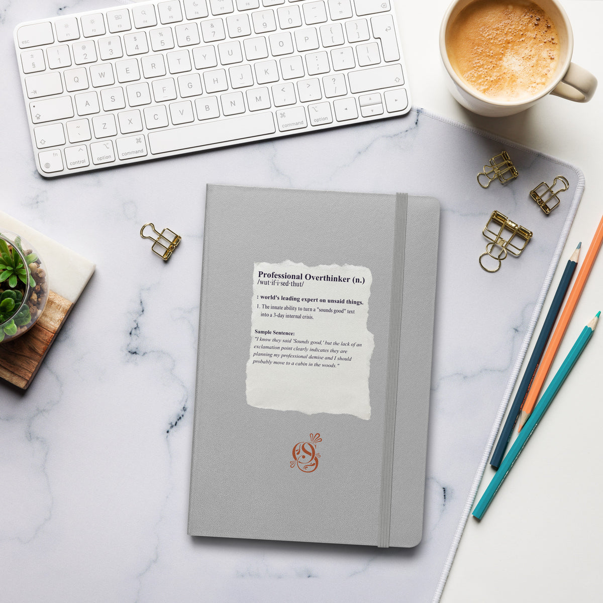Matte silver-gray hardcover notebook on a desk beside a keyboard, coffee cup, and pens.